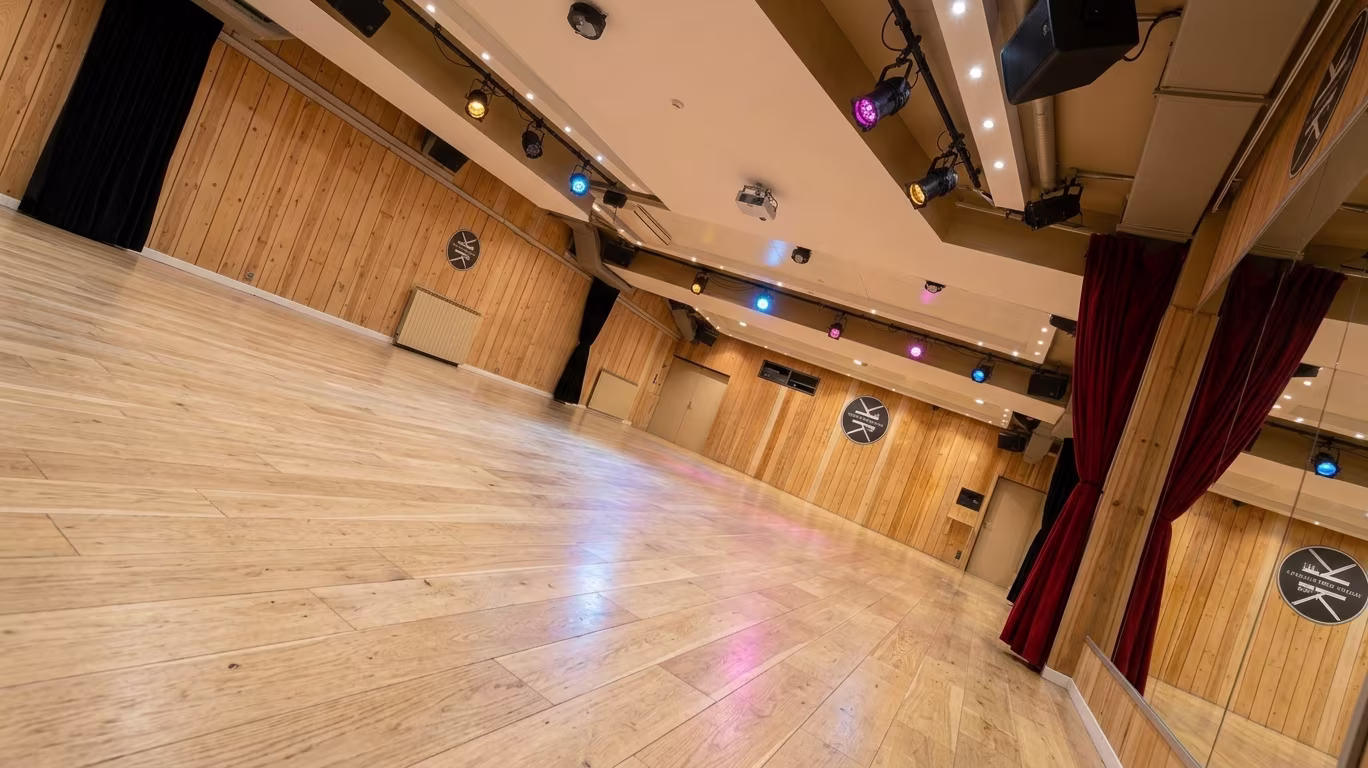 La grande salle du Studio des Rigoles vue d’un angle : parquet, lambris de pin, projecteurs au plafond, rideaux rouges de part et d’autre des miroirs.