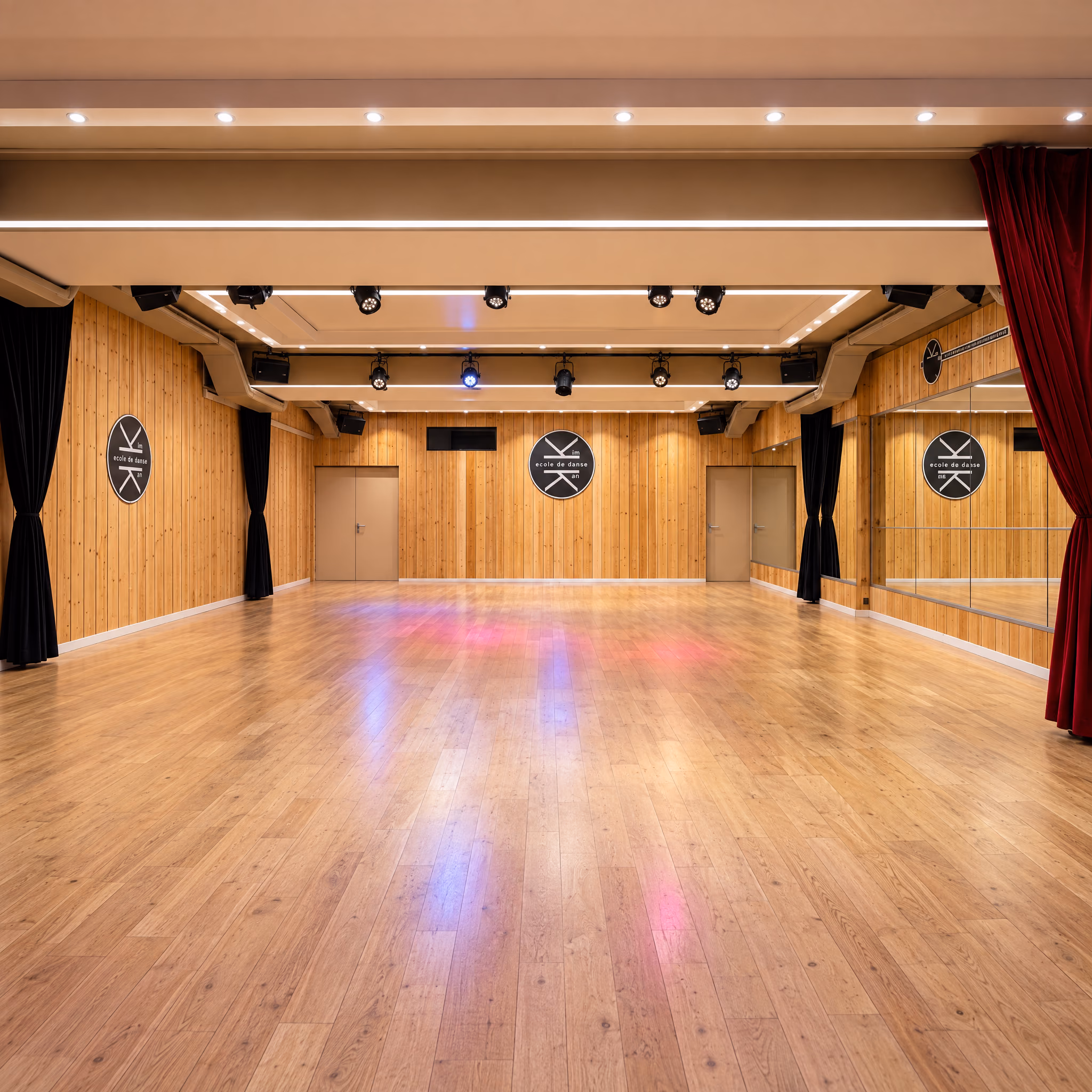 Grande salle de 150 m² du Studio des Rigoles, vide : lambris de pin, rideaux noirs, rideau rouge devant les miroirs, rampe de projecteurs et médaillons du logo.