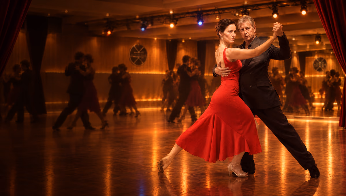 Déclinaison du flyer d’El Baile de los Domingos, le bal de tango de Fuego de Tango : un couple de tango enlacé, elle en longue robe rouge, lui en costume sombre, dans la grande salle du Studio des Rigoles à la lumière ambrée, d’autres couples dansant dans le flou.